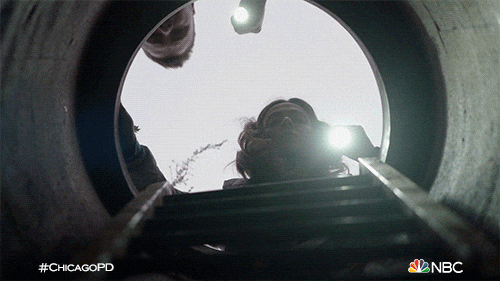 A man and a woman shine a light into a manhole.